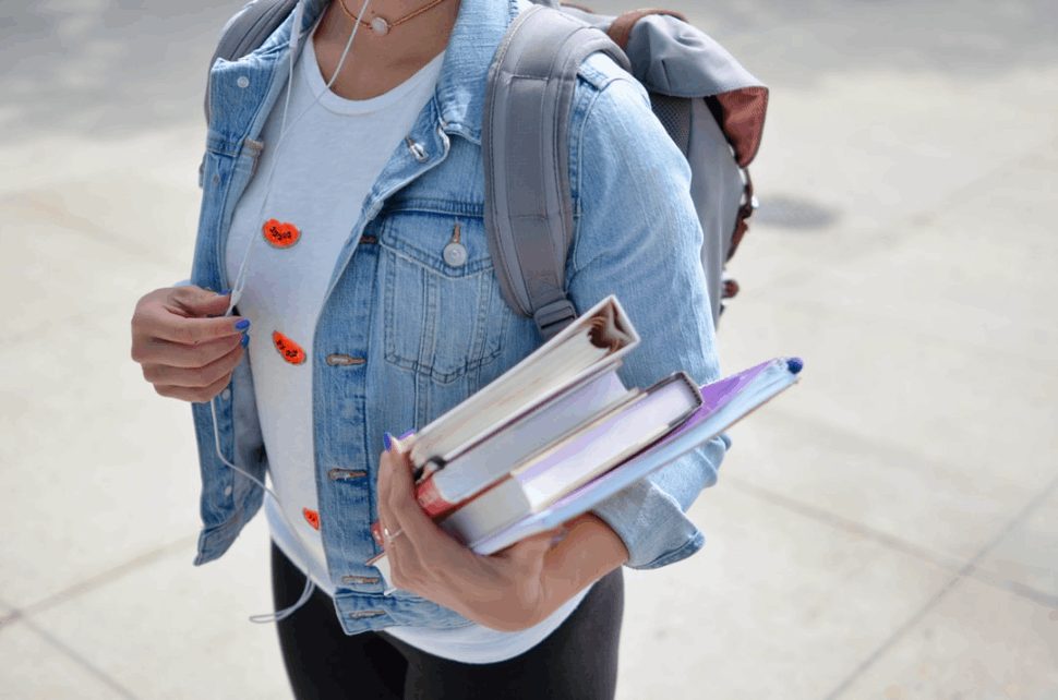woman wearing blue denim jacket and a bag holding books