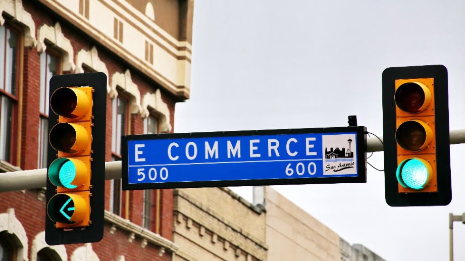 Street sign between two traffic signals that reads e commerce