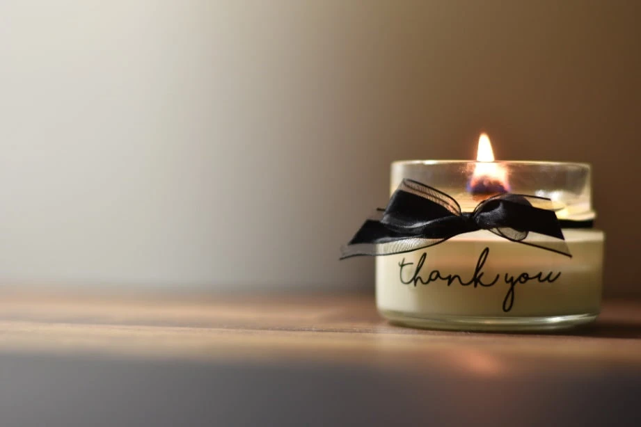 A lit candle with the words thank you written on its glass.