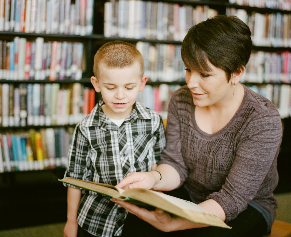 A teacher holding an open book right next to a kid.