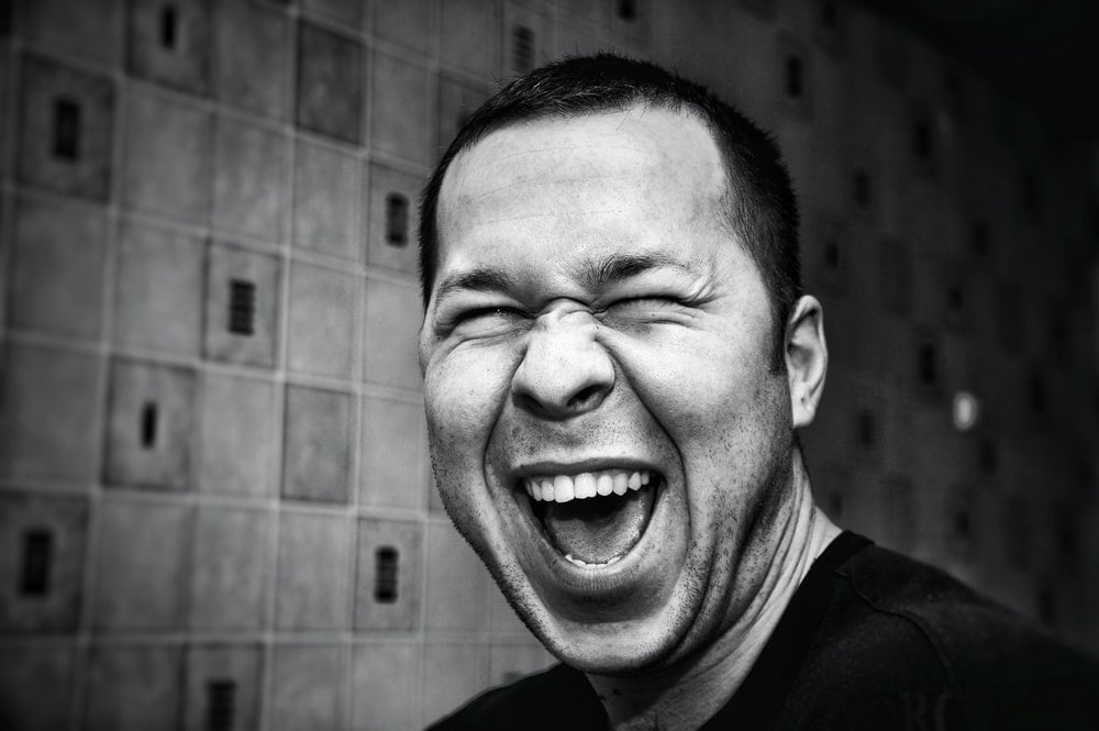 A grayscale picture of a man laughing at the camera.
