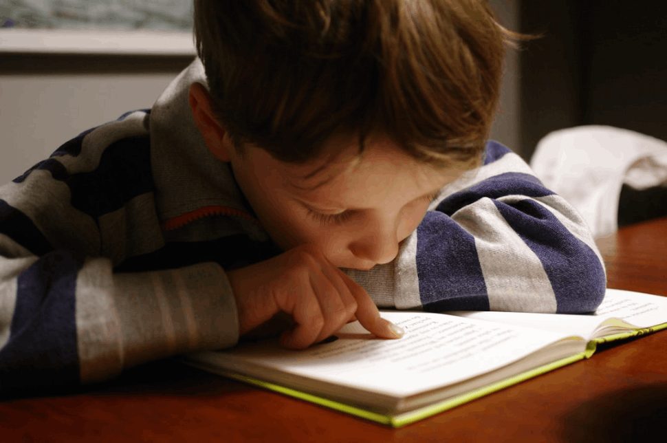 Witness a heartwarming scene: a boy lost in the pages of a book at a wooden desk, embracing knowledge.