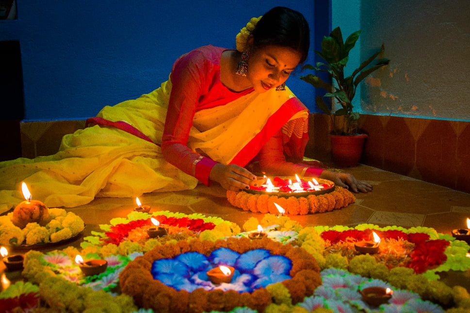 An Indian woman lighting some candles surrounded by colorful flowers.