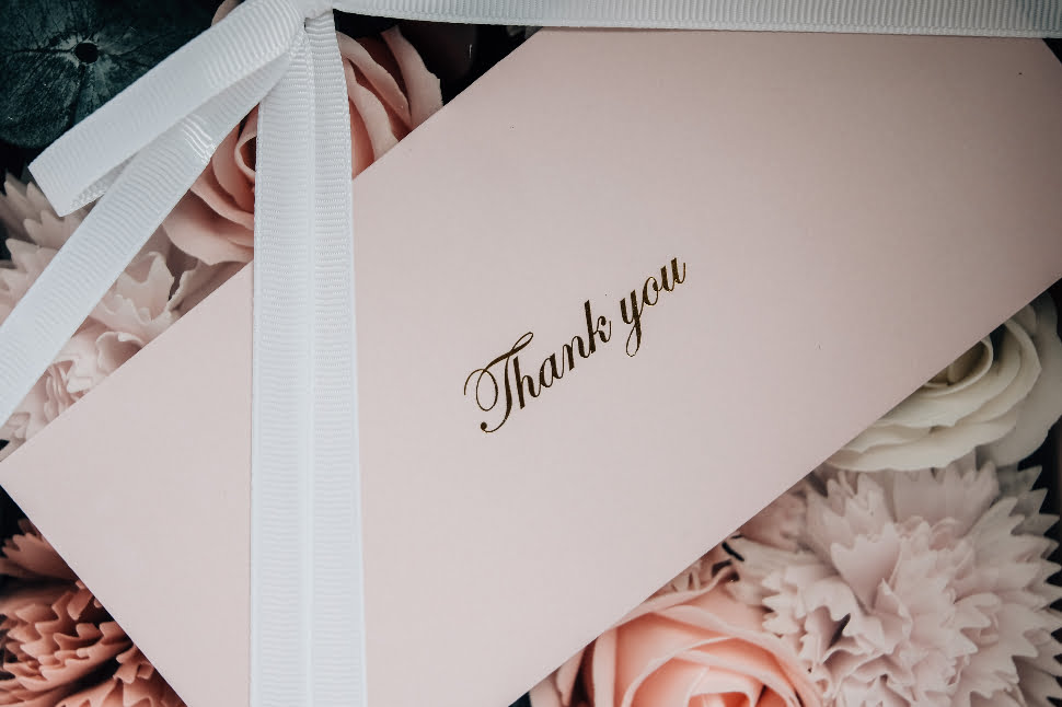 A pink thank you letter with a ribbon and beautiful flowers.