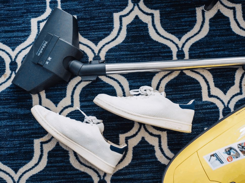 pair of white sneakers beside vacuum cleaner on a blue rug