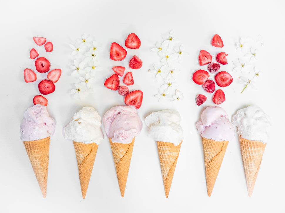 Six ice cream cones with flowers and strawberries above them.