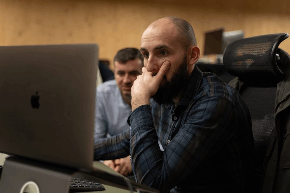 a bald and bearded man looking at a Macbook, looking worried.