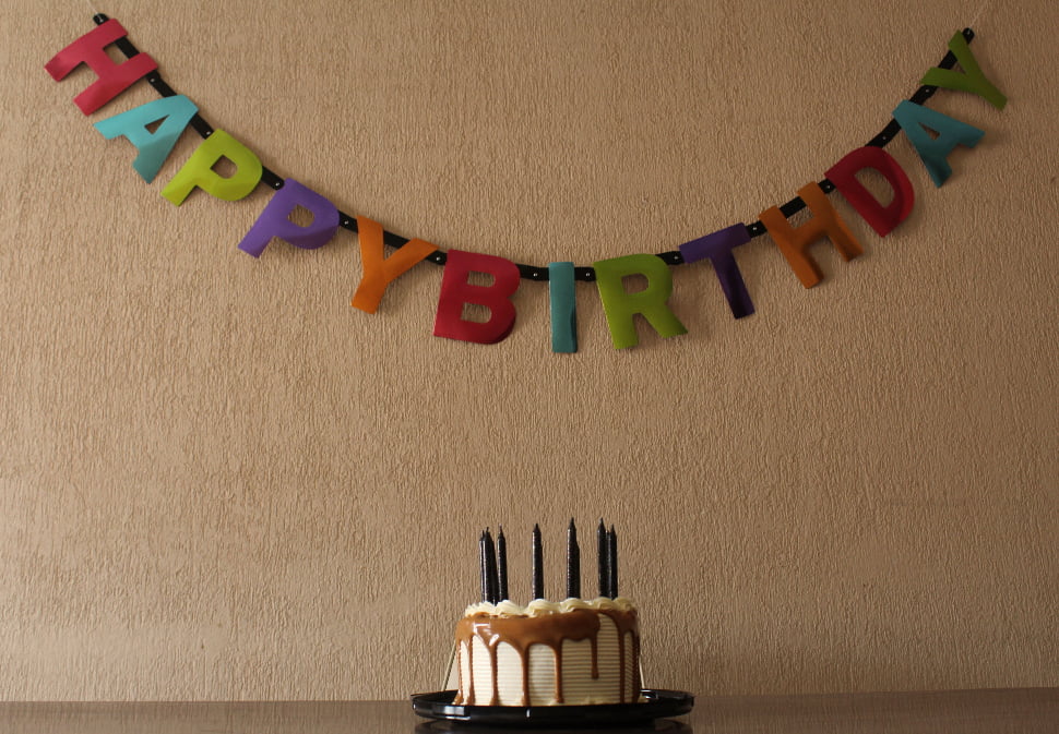 A birthday cake topped with black candles and a Happy Birthday banner in the background.