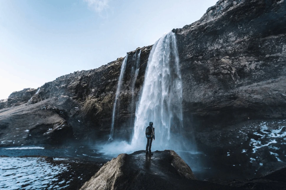 man standing on rock in front of a waterfall during daytime