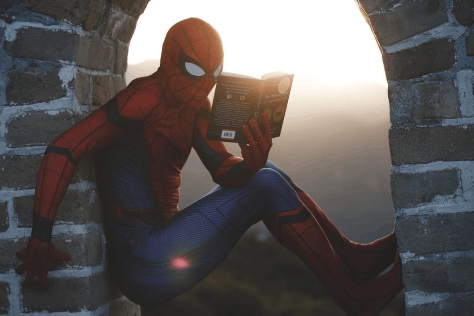 Experience a creative twist: Spiderman reading books while nestled between walls, a balance of heroics and learning.