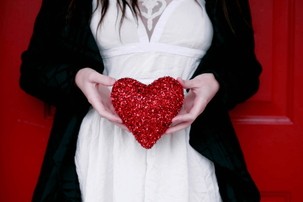 woman in a white dress holding red heart pillow.