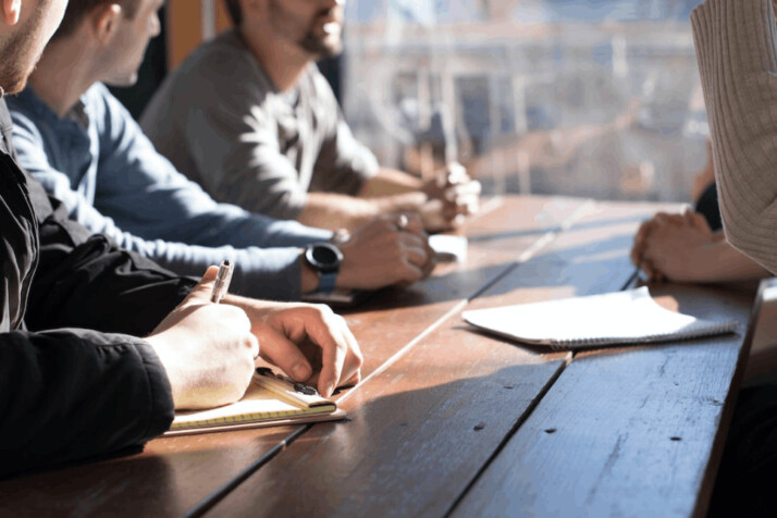 People sitting on chair in front of table while holding pens during daytime