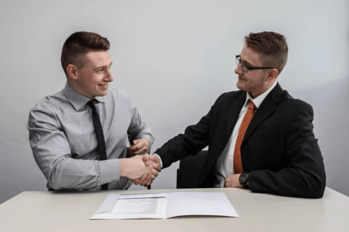 two men facing each other while shake hands and smiling