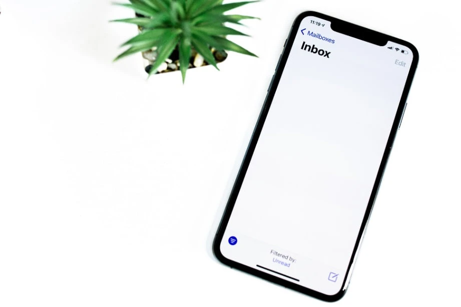 An iPhone, next to a small plant, displaying an email inbox.