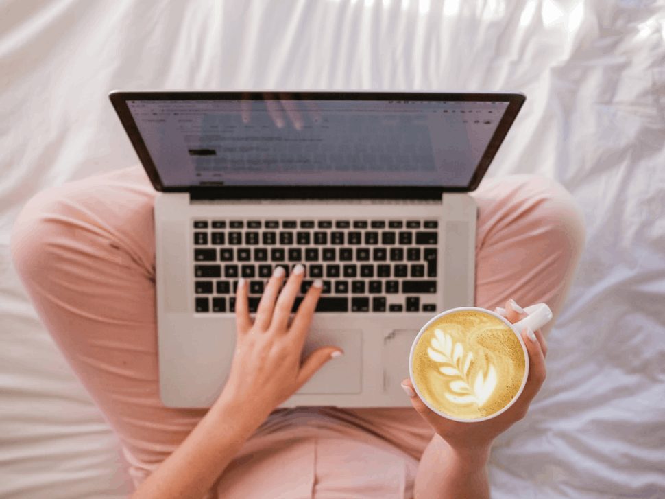 woman in pink pants using MacBook Pro and holding cappuccino