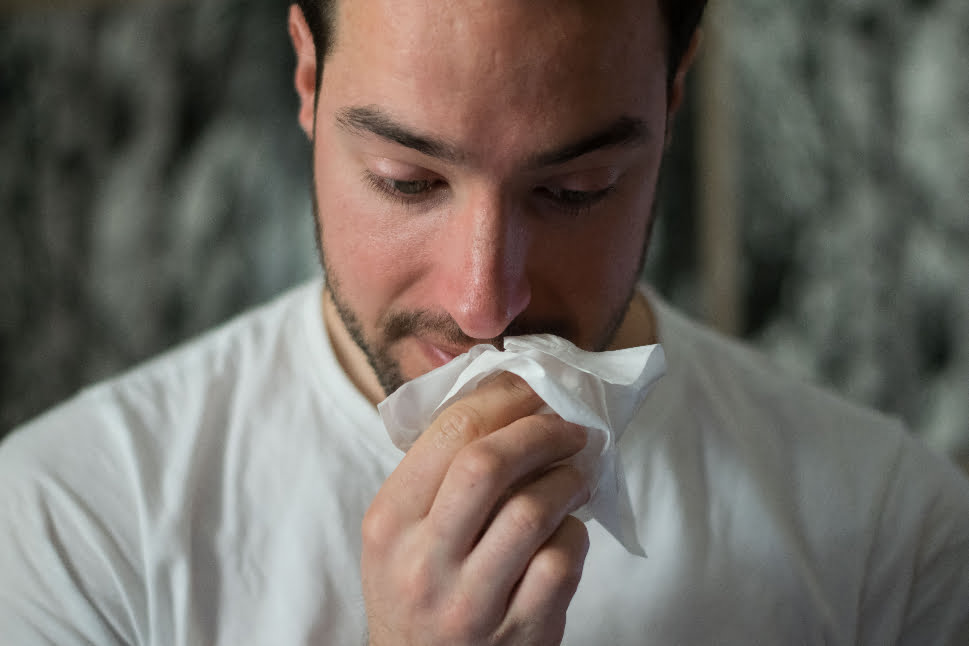 A sick man wiping his nose with a tissue.