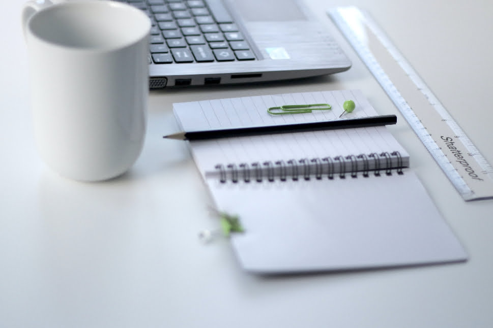 An open notebook next to a mug, laptop, pencil, and ruler.