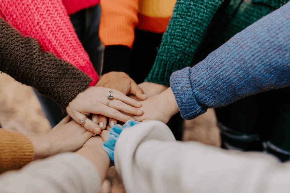 People in sweaters of different colors, holding hands in the center.