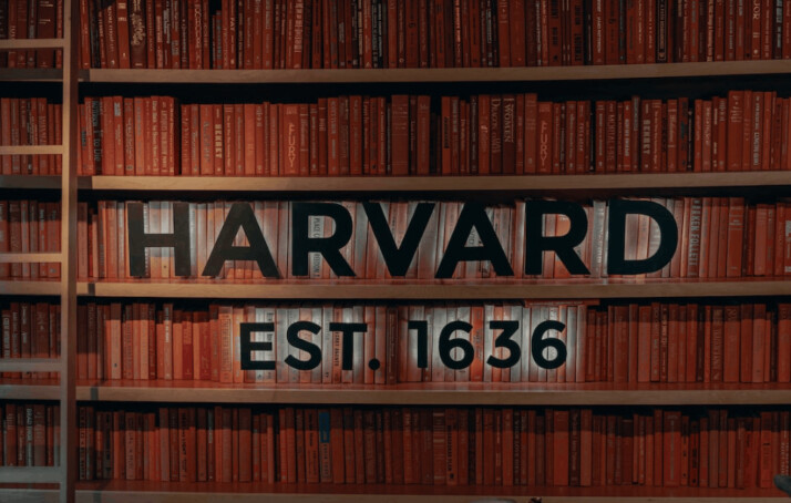 A brown wooden bookshelf on the background with the word Harvard Est. 1636 in black