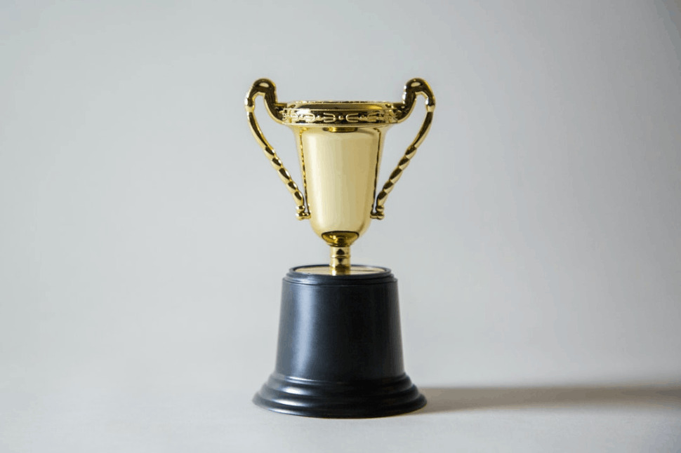 yellow and white trophy on a black stand in front of a white wall