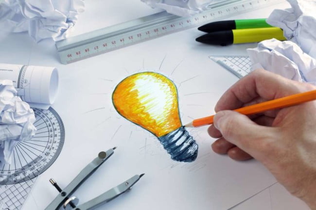 person holding pencil sketching light bulb on white paper