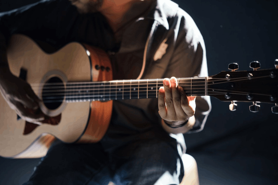 a man wearing a grey shirt playing an acoustic guitar