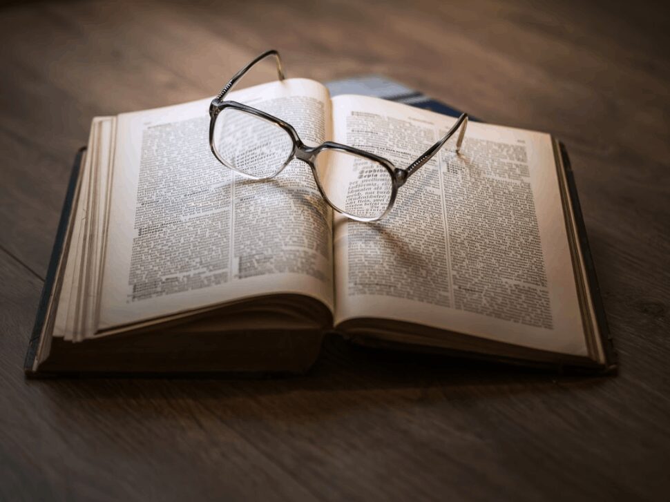 A framed eyeglass placed on top of an open book.