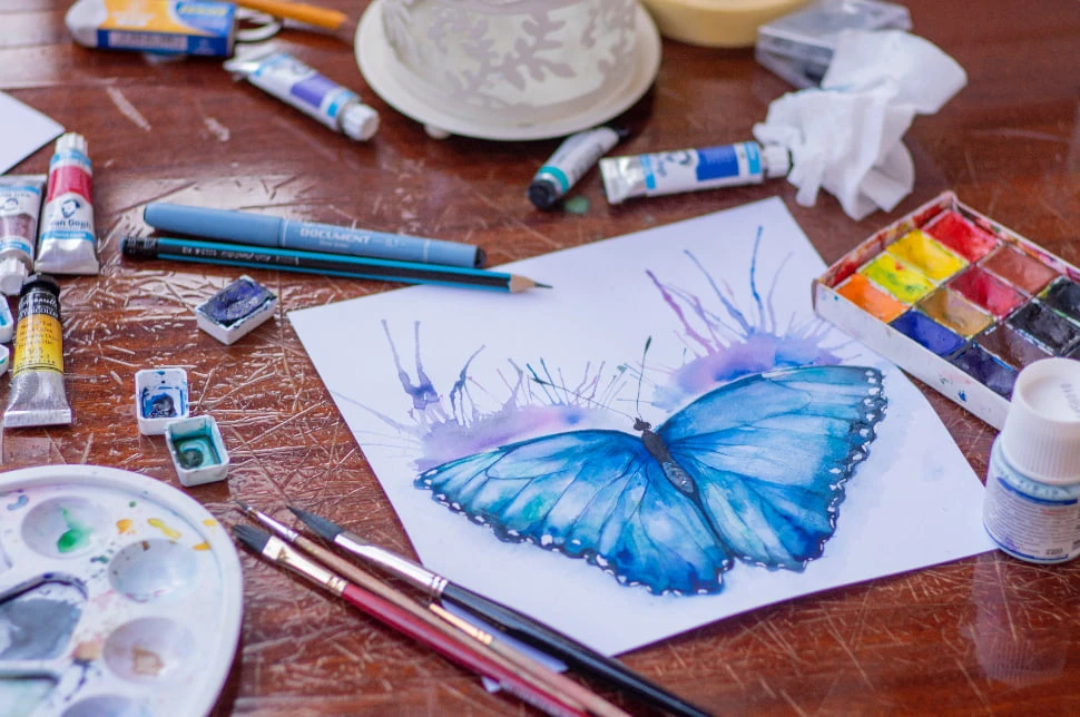 A painting of a blue butterfly surrounded by art materials.
