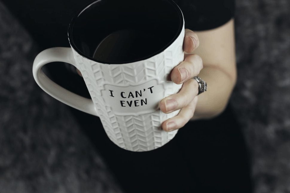 A woman holding a white and black I Can't Even ceramic mug.