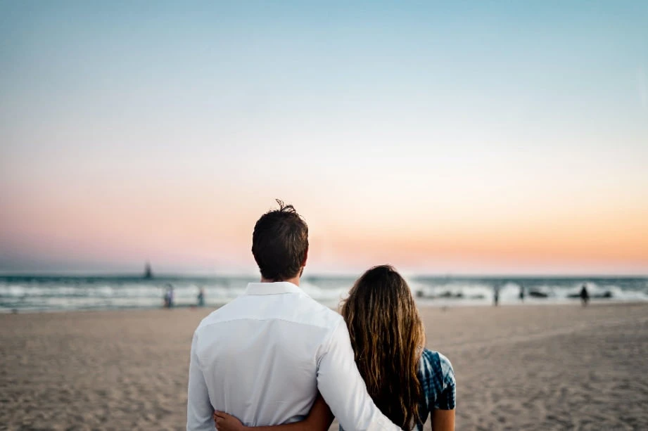 A photo of a couple next to each other, turning towards the beach.