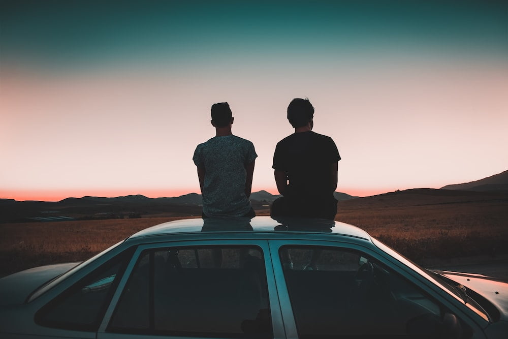 Picture of two men sitting on the roof of a vehicle.