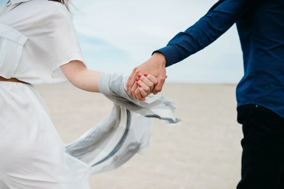 An image of a couple holding hands on the sand