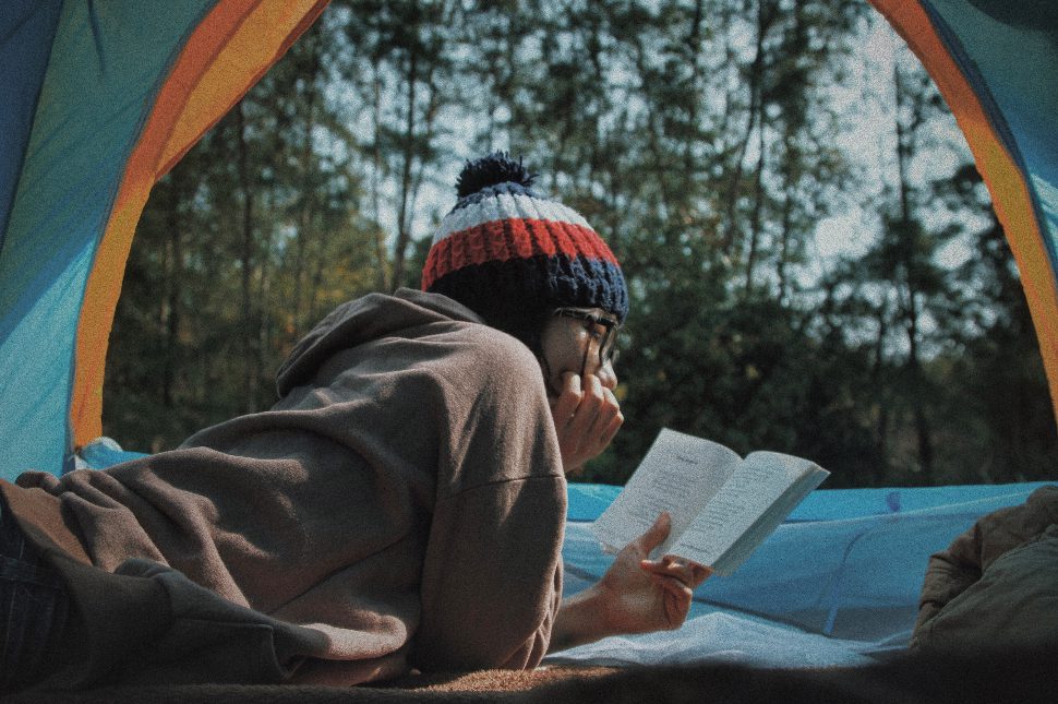 A girl in the wilderness, focused and concentrated on the book that she is reading.