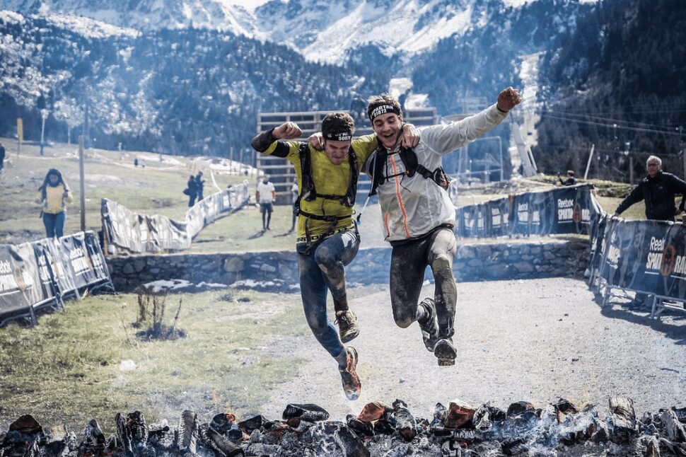 Two Spartan Race participants jumping over burning coal together.