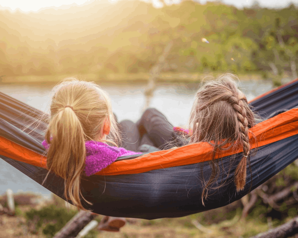 two women lying on hammock next to lake. They are sisters