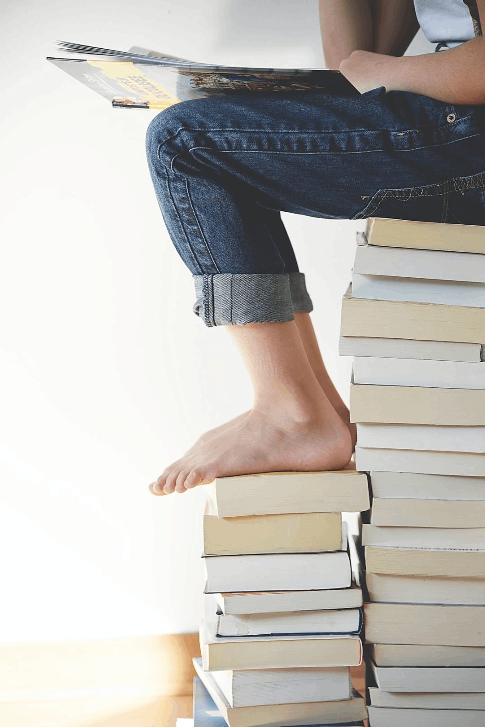 Woman finding a cozy spot on a tower of books, reading with focus