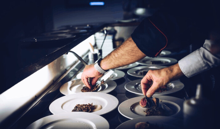 a chef in a black apron preparing a cooked dish