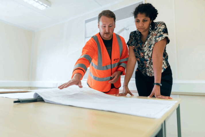 man in orange safety vest beside a woman in black and white floral dress