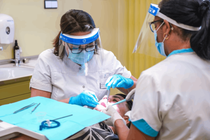 A dentist is treating a patient with the help of a dental assistant