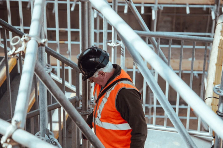 a man standing under scaffoldings wearing a black work helmet.