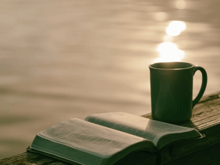 a green ceramic mug placed beside an open book