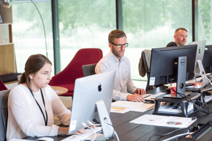 two men and a woman sitting in front of their computers at work. 