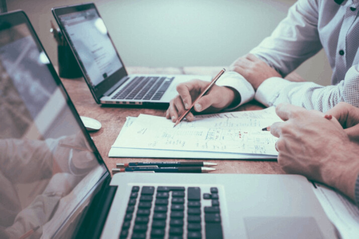 person holding pencil near on white paper near laptop computer