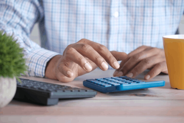 a person using a black keyboard and a blue calculator