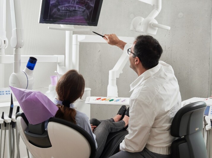 A dentist talking to his patient while pointing to a dental x-ray.