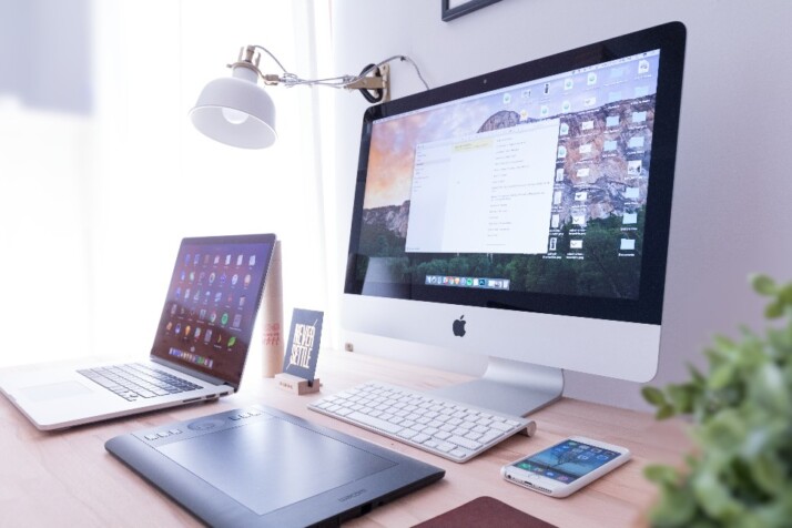 A neat work table with a laptop, computer, a phone.