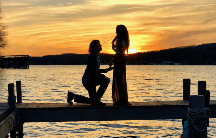 Man kneeling on wooden dock in front of lady during sunset