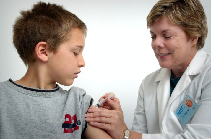 A pediatric nurse pushing an injection on a child's arm.