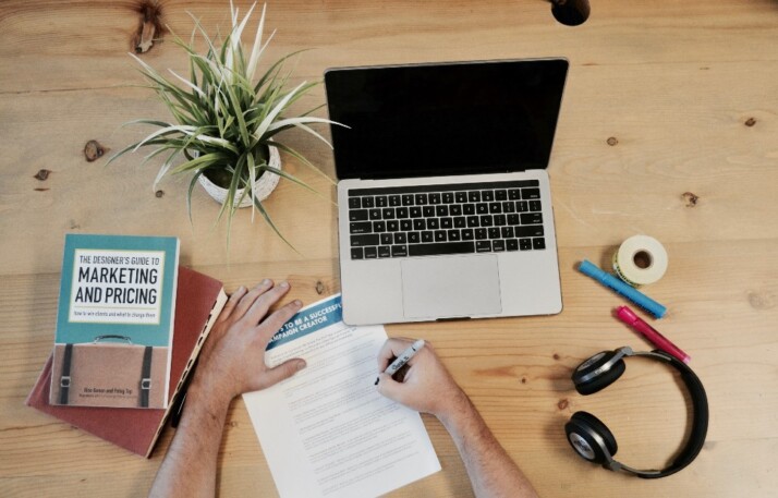 A busy work table with a laptop, headphones, and marketing books.