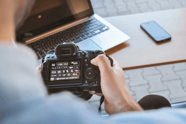 person holding black DSLR camera near silver laptop computer